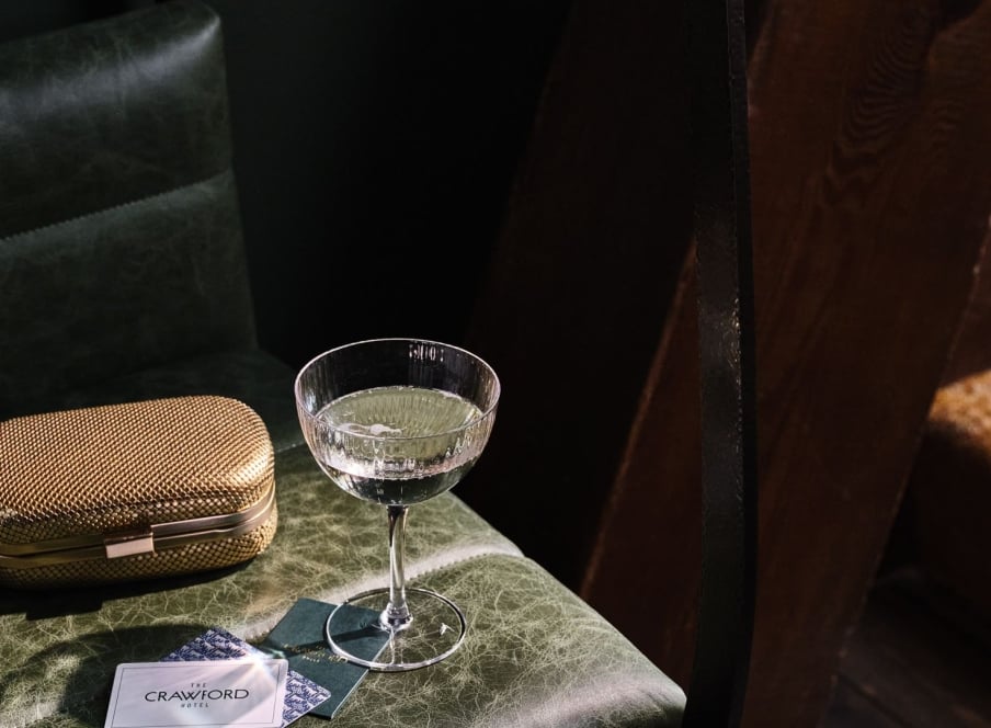 A martini glass on a table with a gold clutch purse.