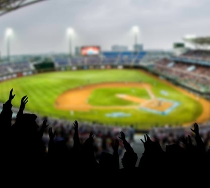 A baseball diamond from the stands. The crowd is cheering with their arms in the air.