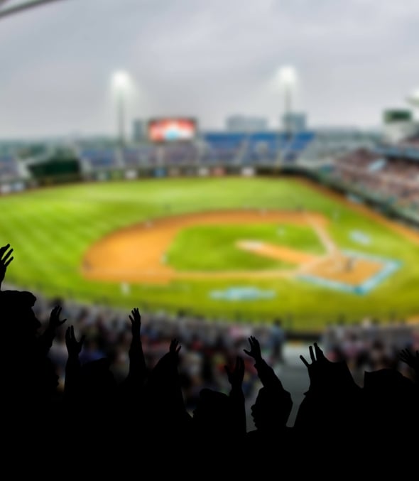 A baseball diamond from the stands. The crowd is cheering with their arms in the air.