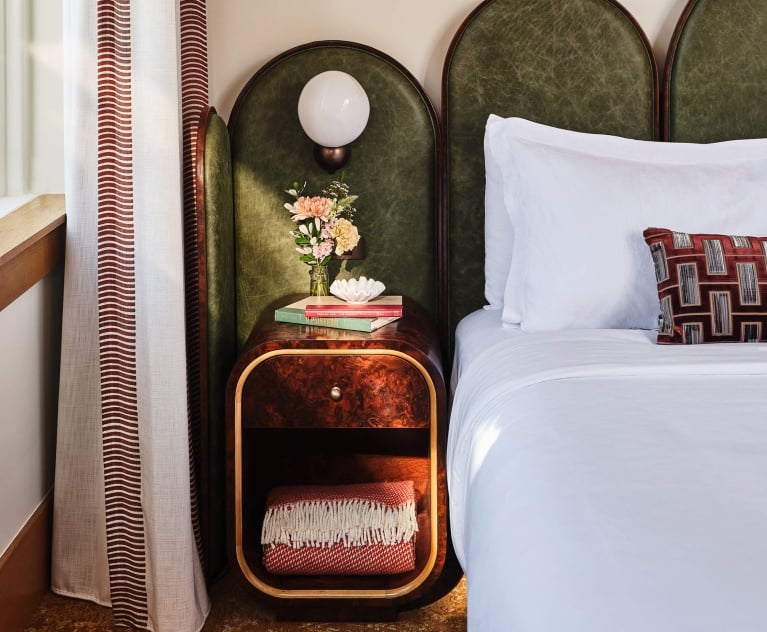 The bedside area of the Deluxe Classic Guest room at the Crawford Hotel in Denver, Colorado. The area has a small table with an extra blanket, fresh cut flowers and a lamp.