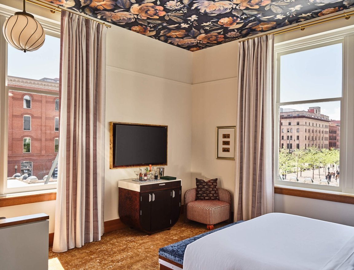 A television, bar cart and chair in the Deluxe Classic Guest room at the Crawford Hotel in Denver, Colorado.