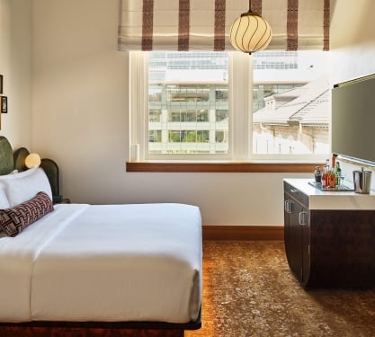 A king bed, bar cart and television in the Superior Classic Guest room at the Crawford Hotel in Denver, Colorado.