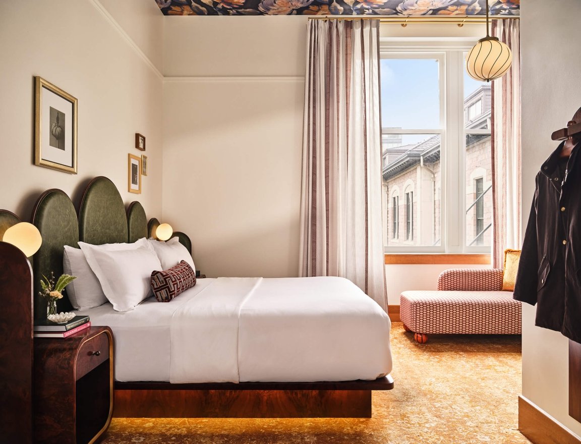 A king bed, side table, coat rack and chaise lounge in the Superior Classic Guest room at the Crawford Hotel in Denver, Colorado.