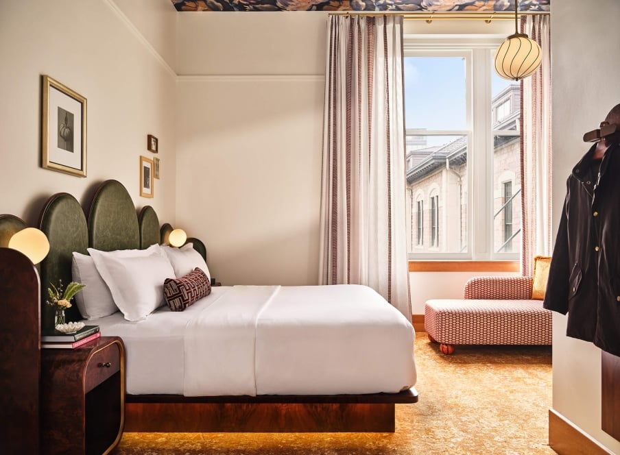 A king bed, side table, coat rack and chaise lounge in the Superior Classic Guest room at the Crawford Hotel in Denver, Colorado.