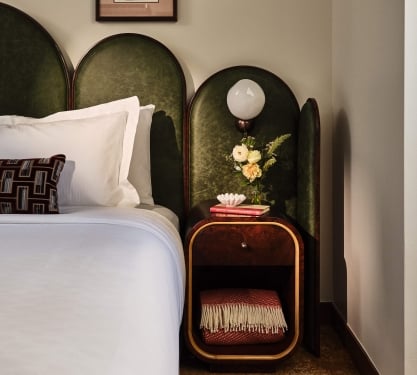 Bedside area with a lamp, side table with extra blanket and fresh cut flowers in the Superior Loft Guest Room at the Crawford Hotel in Denver, Colorado.