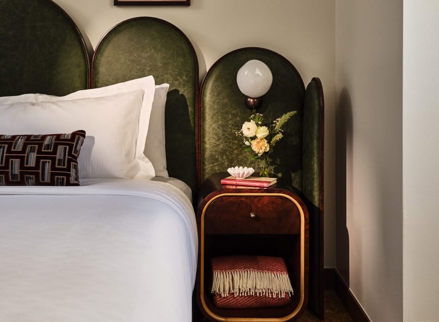 Bedside area with a lamp, side table with extra blanket and fresh cut flowers in the Superior Loft Guest Room at the Crawford Hotel in Denver, Colorado.