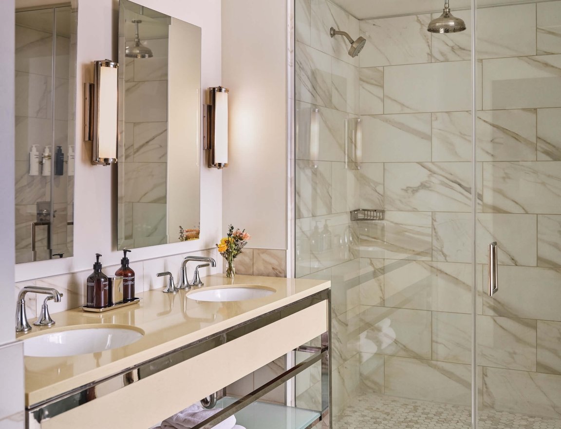 Double sinks and shower of the bathroom in the Premium Loft Guest Room at the Crawford Hotel in Denver, Colorado.