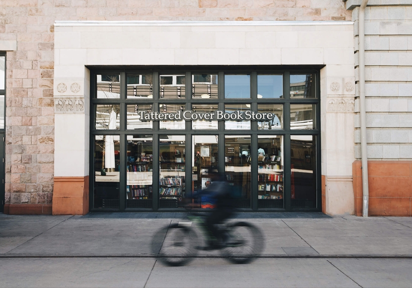 The exterior of Tattered Cover Book Store in Denver, Colorado. A cyclists goes by in a blur.