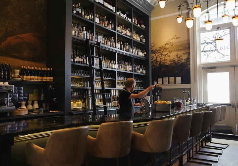 Tall shelving of assorted liquors behind the bar at Ultreia at Union Station in Denver, Colorado. A bar tender prepares drinks.