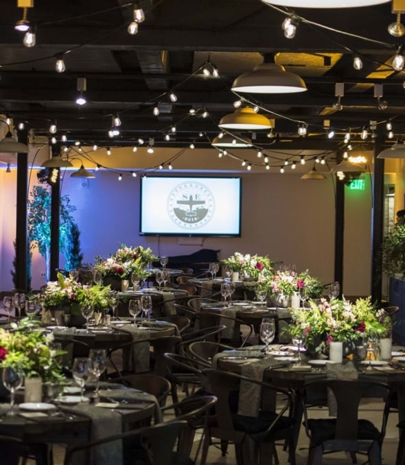 In ambient lighting, tables are set with glassware, tableware and an elegant bouquets of flowers in Webb Gallery at the Crawford Hotel in Denver, Colorado.