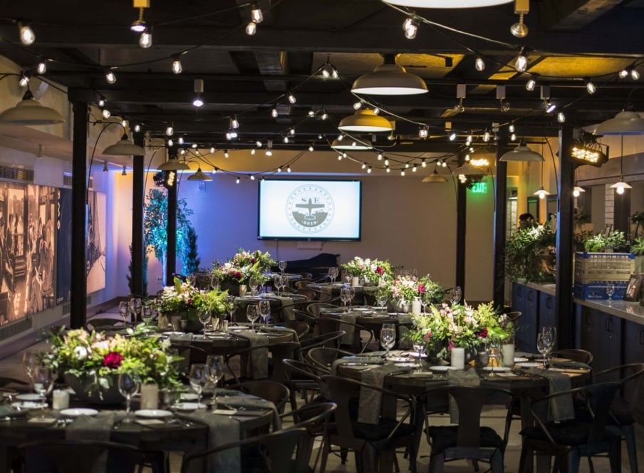 In ambient lighting, tables are set with glassware, tableware and an elegant bouquets of flowers in Webb Gallery at the Crawford Hotel in Denver, Colorado.