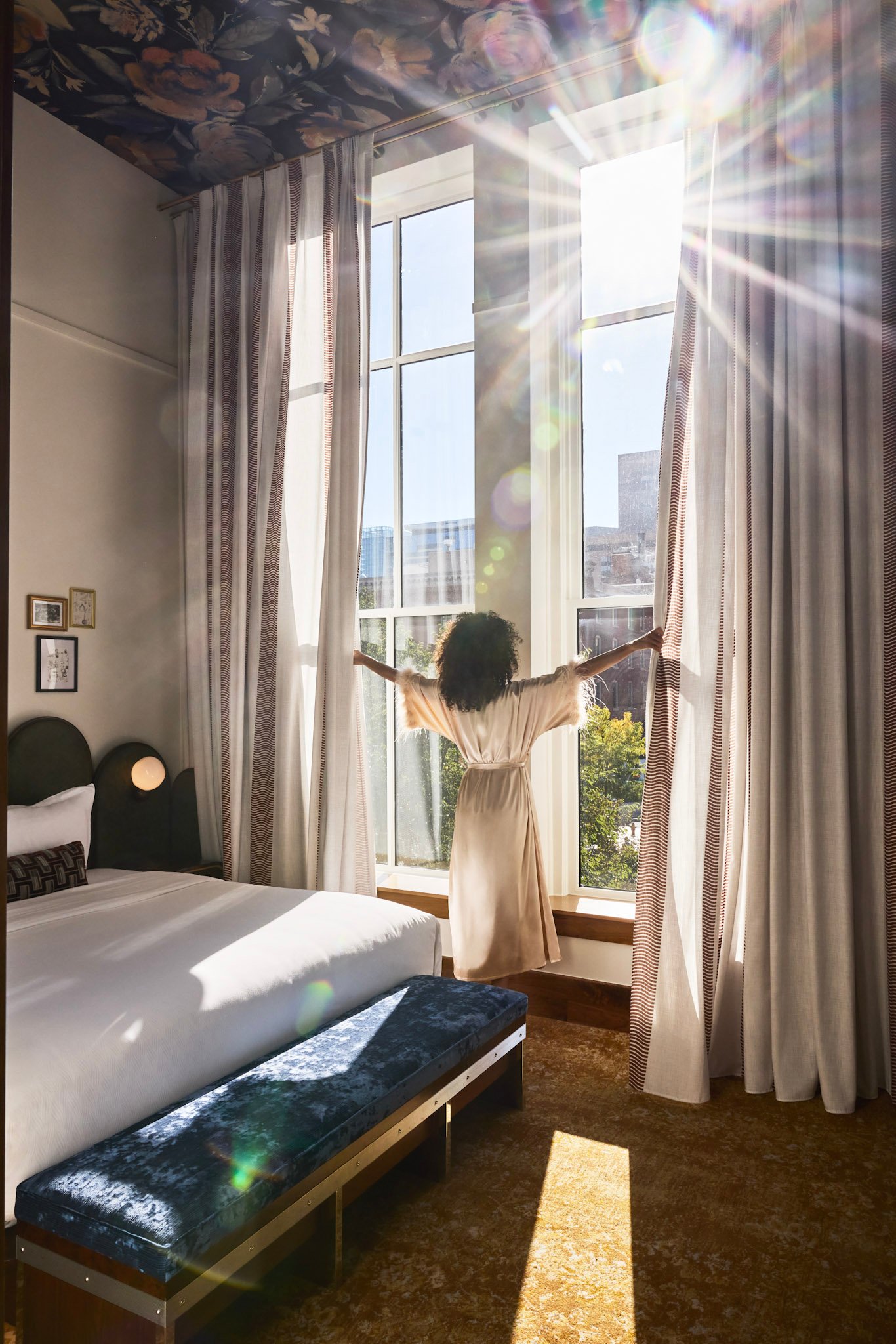 A woman opening her curtains with the sun shinning in