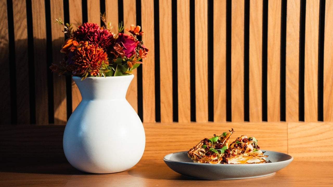 Plate of food on a table next to a vase with flowers